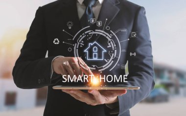 Akıllı ev kontrolünü tablette kullanan eller. Arka planda oturma odasının içi..