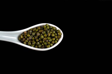 Siyah zemin üzerinde yeşil soya ile dolu beyaz seramik kaşık..
