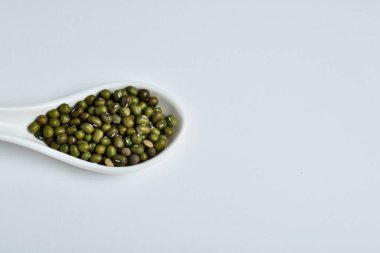 Beyaz arka planda yeşil soya ile dolu beyaz seramik kaşık.