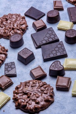 Stüdyoda çekilen çeşitli çikolata ürünleri açık gri arka planda beyaz dokuya sahip. Koyu çikolata, sütlü çikolata, beyaz çikolata, çikolatalı kurabiye, çikolata.