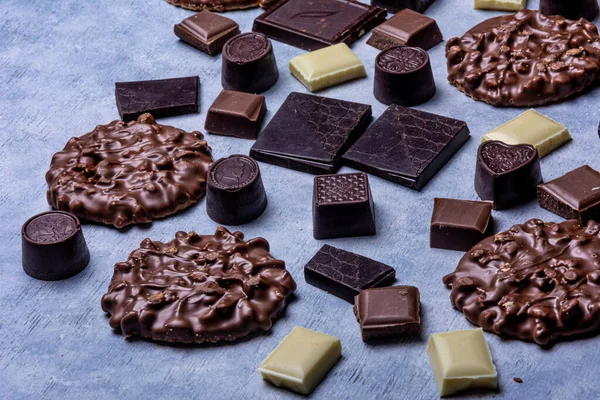 Variety of chocolate products photographed in studio on a light grey background with white texture. Dark chocolate, milk chocolate, white chocolate, chocolate-dipped cookies, chocolates