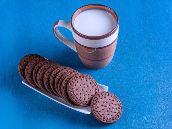 Cup of milk with cocoa cookies on a white tray. Study photo on blue background hand painted by photographer