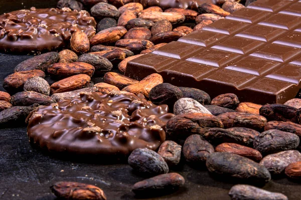 Milk chocolate tablet accompanied by cookies dipped in chocolate and different ingredients.
