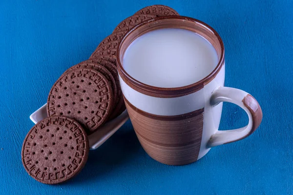 Cup of milk with cocoa cookies on a white tray. Study photo on blue background hand painted by photographer