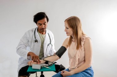 Hintli bir asyalı doktor, beyaz önlük giymiş, Avrupalı bir kadının tansiyonunu ölçüyor..