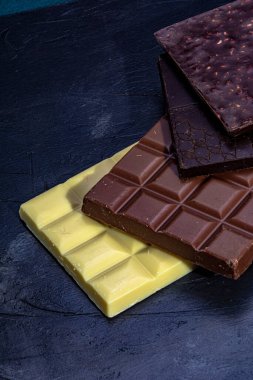Koyu arkaplanda üç çikolata. Siyah çikolata tabletleri, beyaz ve sütlü, eskimiş görünümün koyu arka planında.