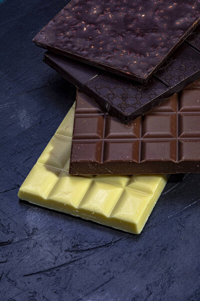 Three chocolates in dark background. Black chocolate tablets, with milk and white, on a dark background of vintage appearance.
