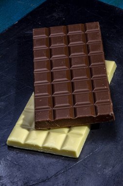 Siyah bir masada beyaz çikolata ve sütlü çikolata tabletleri. Durgun hayat.