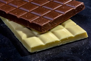 Siyah bir masada beyaz çikolata ve sütlü çikolata tabletleri. Durgun hayat.