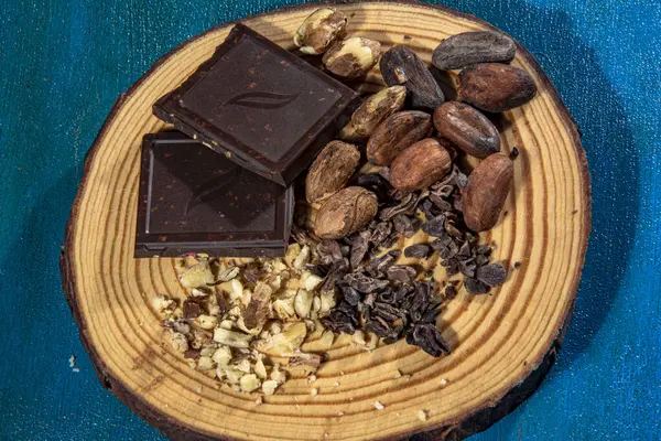 黒チョコレートにヘーゼルナッツをトランクのスライスにテクスチャブルーの背景に置きます ヘーゼルナッツ ローストココア豆 チョコレートチップが添えられています — ストック写真
