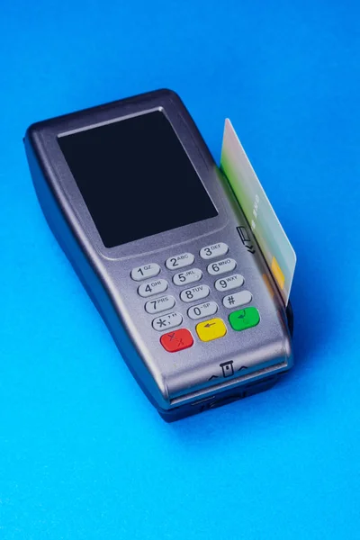 Credit card reader with a credit card inserted in the side slot, studio shot on medium blue background. Simulated card, imaginary logo.