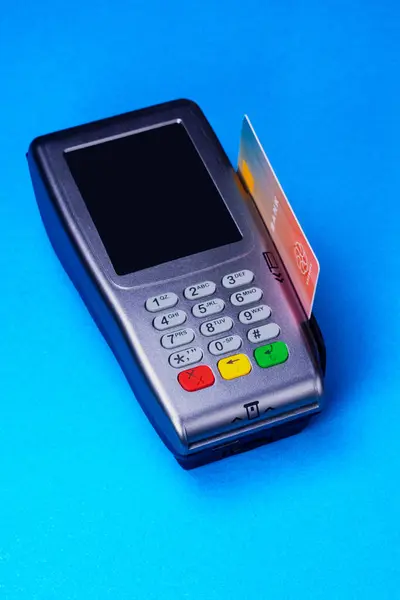 Credit card reader with a credit card inserted in the side slot, studio shot on medium blue background. Simulated card, imaginary logo.