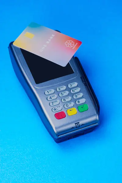 Credit card reader with a card on the screen, studio shot on blue background. Simulated card, imaginary logo.