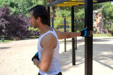 Parkta bir adam kollarını uzatıyor. Adamın saati ve mavi ve siyah bir eldiveni var.