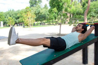 Bir kadın parkta bir bankta bacak kaldırma hareketi yapıyor. Gülümsüyor ve eğleniyor.