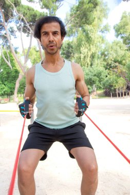 Bir adam yeşil gömlek giyerken halat çekiyor. Olay yeri açık ve o bir park.