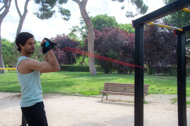 Bir adam direniş grubuyla egzersiz yapıyor. Yeşil bir atlet giyiyor ve kollarını kavuşturuyor.