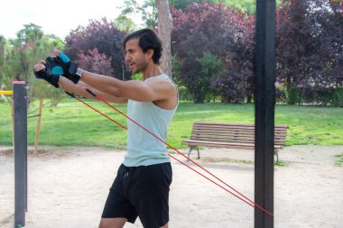 Bir adam direniş grubuyla egzersiz yapıyor. Yeşil bir atlet giyiyor ve kollarını kavuşturuyor.