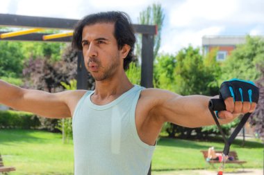 Bir adam direniş grubuyla egzersiz yapıyor. Yeşil bir atlet giyiyor ve kollarını kavuşturuyor.