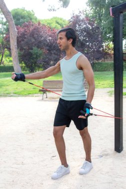 Bir adam direniş grubuyla egzersiz yapıyor. Yeşil bir atlet giyiyor ve kollarını kavuşturuyor.