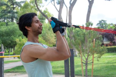 Bir adam direniş grubuyla egzersiz yapıyor. Yeşil bir atlet giyiyor ve kollarını kavuşturuyor.