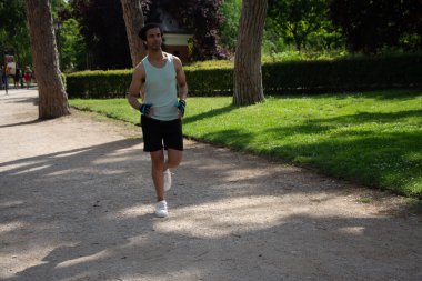 Yeşil bir geçmişi olan bir adam parkta koşuyor. Yeşil bir atlet ve siyah bir şort giyiyor.