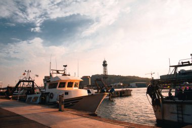 Gün batımında Barcelona Balıkçılık Limanı 'na yanaşan balıkçı teknelerinin görüntüsü. Arka planda ikonik kule var. Sahne, limanın deniz atmosferini yakalıyor..