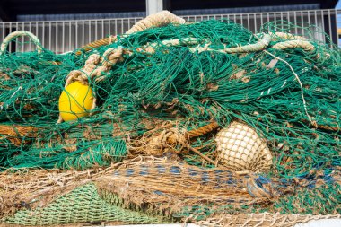 Halat ve deniz donanımına dolanmış yeşil balık ağları ve sarı şamandıralar. Resim, temel balıkçılık malzemelerinin karmaşık detaylarını ve dokularını vurgular..
