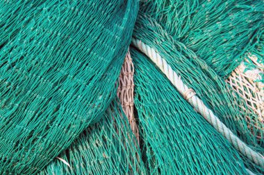 Yeşil balık ağlarının bej ve beyaz halatlarla yakın plan çekimleri, ticari balıkçılık için gerekli olan ayrıntılı doku ve düğümleri vurguluyor.