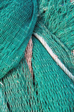 Yeşil balık ağlarının bej ve beyaz halatlarla yakın plan çekimleri, ticari balıkçılık için gerekli olan ayrıntılı doku ve düğümleri vurguluyor.