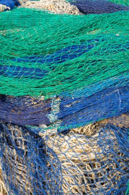 Stack of green, blue, and yellow fishing nets forming a colorful pattern in a coastal setting. clipart