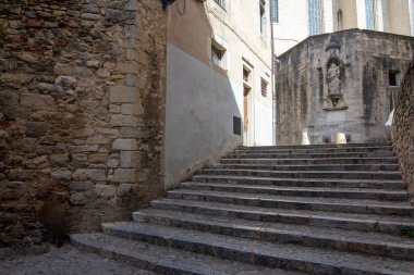 Eski Girona kasabasında taş basamaklar, tarihi bir kiliseye doğru gidiyor, bir heykel ve antik mimari sergileniyor..