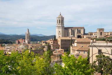 Girona 'nın tarihi binaları çevreleyen katedrali ve dağlık bir zemin üzerindeki yemyeşil ağaçları gösteren manzarası..