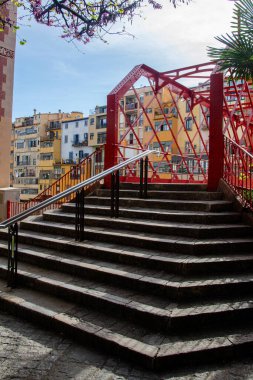 Girona 'daki kırmızı Pont de les Peixateries Velles köprüsüne çıkan merdiven, açık bir gökyüzünün altındaki renkli binalarla çevrili..