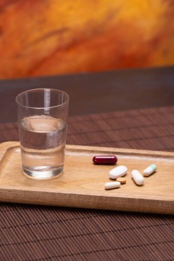 A wooden tray containing pills and a glass of water, emphasizing the importance of daily medication and hydration for health care. clipart