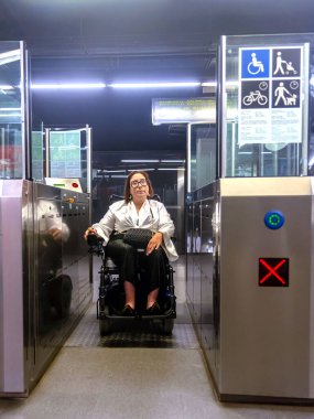 Tekerlekli sandalyedeki kadın metro istasyonundan çıkmak için ulaşılabilir bir kapı kullanıyor. Bu da toplu taşıma seçeneklerini gösteriyor..