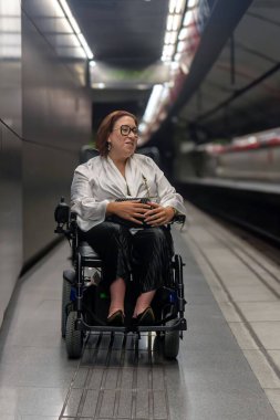 Kadın tekerlekli sandalye kullanıcısı bir metro platformunda bekliyor. Toplu taşımacılıkta erişilebilirlik ve kapsayıcı tasarımı yansıtıyor..