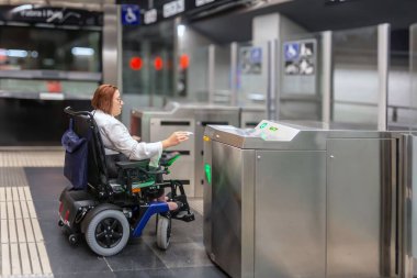 Elektrikli tekerlekli sandalyedeki kadın ulaşılabilir bir turnikeden metroya ulaşmak için geçiş kartı kullanıyor..