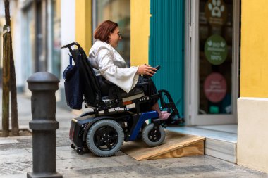 Bir kadın, mağazaya girmek için elektrikli sandalyesiyle rampa kullanır. Erişilebilirlik çözümleri sunar..