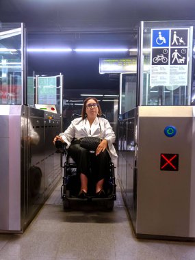 Tekerlekli sandalye kullanıcısı metro sistemine erişilebilir bir kapıdan giriyor ve toplu taşımanın önemini gözler önüne seriyor..