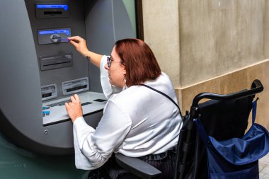 Elektrikli sandalyedeki bir kadın, halka açık yerlerde ulaşılabilir bankacılığın önemini vurgulayarak ATM 'ye giriyor..