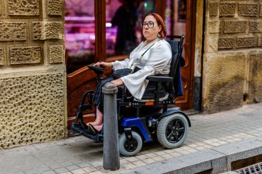 Tekerlekli sandalyedeki bir kadın dar bir şehir kaldırımında, ulaşılabilirlik çözümlerinin eksikliğini vurgulayan bir Bollard ile karşı karşıya geliyor..