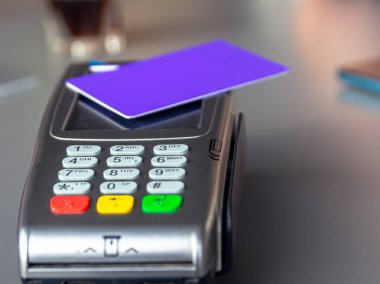 A close-up of a purple credit card on a payment terminal, illustrating a contactless payment. clipart