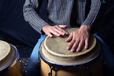 Bir konser sırasında konga davulu çalan müzisyenlerin yakın çekimi. El hareketine ve davul dokusuna odaklan.