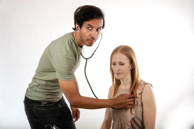 Genç bayan doktor, normal giyinmiş, kalbini dinliyor..