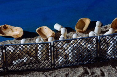 Wooden figures behind a fence on a sandy shore, with boats symbolizing journeys, representing migration challenges and human resilience. clipart