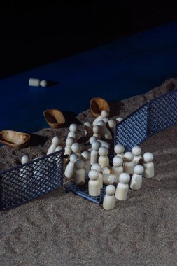 Wooden figurines and small boats on sandy terrain divided by fences, symbolizing migration struggles and border challenges. clipart