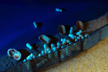 Wooden figures and boats set on sandy terrain behind a metal fence, illuminated by cool tones of blue, representing themes of separation and migration. clipart