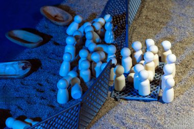 A surreal arrangement of wooden boats and grouped figurines near a glowing fence on sand. clipart