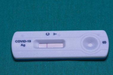 Close-up of a COVID-19 antigen rapid test cassette displaying a single control line, indicating a negative result, on a teal background. clipart